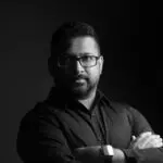 Monochrome portrait of a man with glasses and beard, exuding confidence.